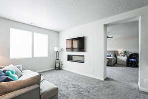 Carpeted living area with baseboards, a textured ceiling, and a glass covered fireplace