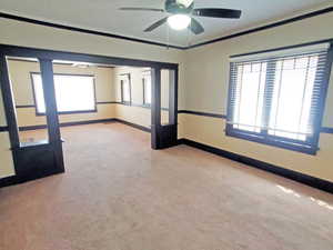 Carpeted spare room featuring baseboards, ornamental molding, and a ceiling fan