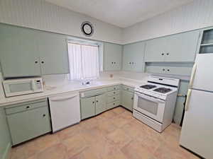 Kitchen with a sink, white appliances, green cabinets, and light countertops