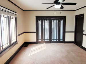 Carpeted empty room with crown molding, a healthy amount of sunlight, and ceiling fan