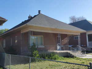 Rear view of house with a porch, brick siding, fence, and roof with shingles