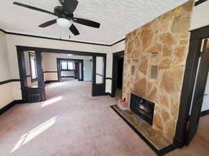 Unfurnished living room with carpet, visible vents, a fireplace, ornamental molding, and a textured ceiling