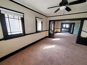 Empty room featuring baseboards, carpet floors, wallpapered walls, a textured ceiling, and crown molding