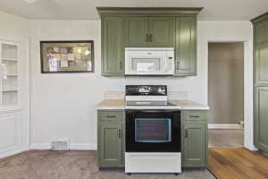 Kitchen featuring white microwave, visible vents, green cabinetry, electric range, and tile counters
