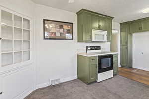 Kitchen with white microwave, light countertops, carpet flooring, electric range, and green cabinetry