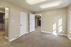 Unfurnished bedroom featuring carpet, baseboards, visible vents, arched walkways, and a textured ceiling