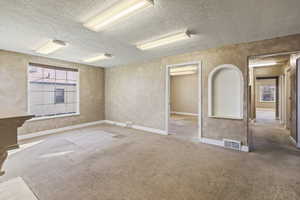 Carpeted empty room featuring visible vents, a textured ceiling, and baseboards