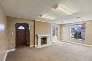 Unfurnished living room with carpet flooring, a fireplace with flush hearth, baseboards, and arched walkways