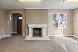 Unfurnished living room with a textured ceiling, arched walkways, carpet flooring, baseboards, and a tile fireplace
