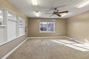 Carpeted spare room featuring ceiling fan, baseboards, visible vents, and a textured ceiling