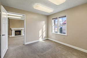Empty room with baseboards, a fireplace with flush hearth, a textured ceiling, and carpet flooring