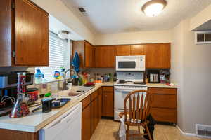 Kitchen with white appliances, visible vents, brown cabinets, light countertops, and a sink