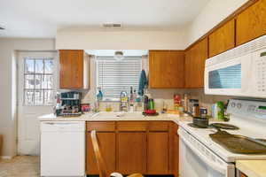 Kitchen with brown cabinets, light countertops, visible vents, a sink, and white appliances