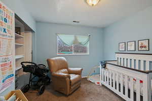 Bedroom featuring a nursery area, visible vents, carpet flooring, and a textured ceiling