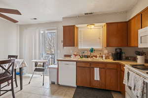 Kitchen with white appliances, brown cabinetry, a sink, and visible vents