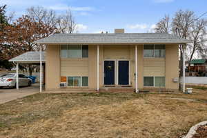 Raised ranch featuring brick siding, a shingled roof, an attached carport, driveway, and a front lawn