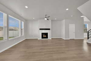 Unfurnished living room with a glass covered fireplace, recessed lighting, light wood finished floors, a ceiling fan, and stairway