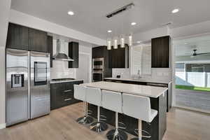 Kitchen featuring modern cabinets, stainless steel appliances, a kitchen bar, decorative light fixtures, and light wood-style flooring