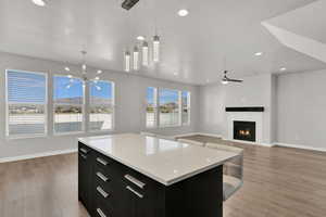 Kitchen featuring dark cabinetry, pendant lighting, recessed lighting, a lit fireplace, and light wood-style flooring