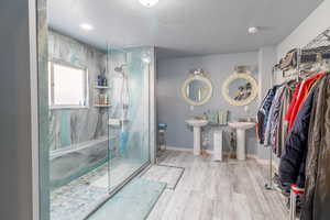 Full bathroom with a marble finish shower, baseboards, wood finished floors, a textured ceiling, and a sink