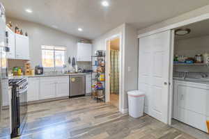 Kitchen featuring lofted ceiling, separate washer and dryer, white cabinetry, appliances with stainless steel finishes, and light wood-type flooring