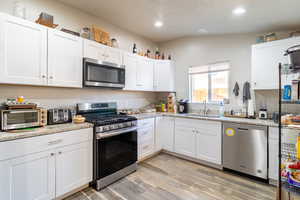 Kitchen with appliances with stainless steel finishes, white cabinets, a sink, and light wood-style flooring