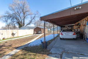 View of vehicle parking featuring a storage shed, a carport, fence, and driveway