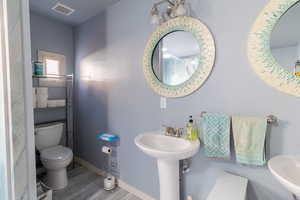 Half bathroom with toilet, a sink, visible vents, wood finished floors, and baseboards