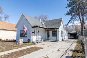 Bungalow featuring a porch, concrete driveway, roof with shingles, and fence