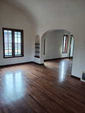 Unfurnished room with dark wood-type flooring, baseboards, arched walkways, and visible vents