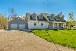 Cape cod-style house with a porch, a front lawn, an outbuilding, driveway, and a chimney