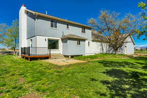 Back of property featuring a lawn, a deck, stucco siding, and a chimney
