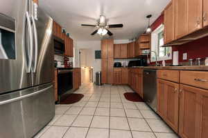 Kitchen with light tile patterned floors, open shelves, dark countertops, appliances with stainless steel finishes, and brown cabinetry