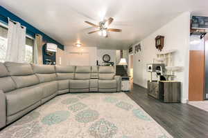 Living room with dark wood-style floors, a ceiling fan, and baseboards