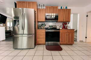 Kitchen with stainless steel appliances, dark countertops, brown cabinetry, and light tile patterned floors