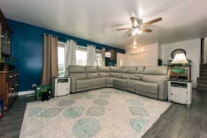 Living area with a ceiling fan, stairs, baseboards, and dark wood-type flooring