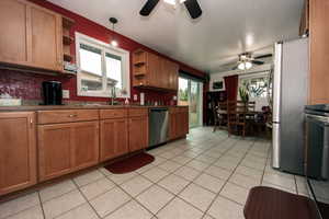 Kitchen featuring brown cabinetry, appliances with stainless steel finishes, open shelves, and light tile patterned flooring