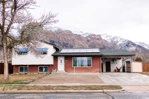 Tri-level home featuring entry steps, an outbuilding, a mountain view, solar panels, and brick siding