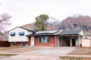 Tri-level home featuring driveway, brick siding, solar panels, and fence