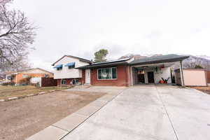 Tri-level home featuring brick siding, a storage unit, concrete driveway, fence, and an outdoor structure