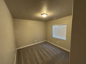 Spare room featuring baseboards, visible vents, dark carpet, and a textured ceiling