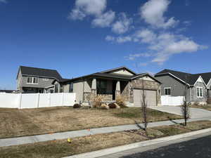 View of front of home featuring fence, an attached garage, covered porch, concrete driveway, and stone siding