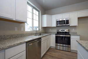 Kitchen featuring a sink, light stone counters, dark wood-style floors, white cabinetry, and appliances with stainless steel finishes