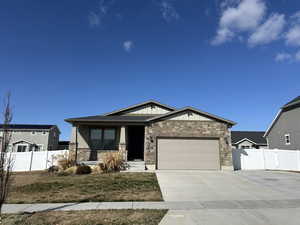 Craftsman-style house featuring fence, an attached garage, concrete driveway, stone siding, and board and batten siding