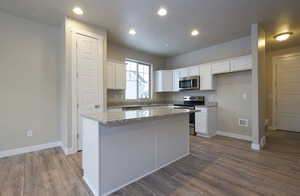 Kitchen with baseboards, a kitchen island, dark wood finished floors, white cabinets, and appliances with stainless steel finishes