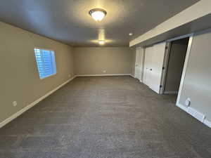 Unfurnished bedroom featuring baseboards, visible vents, dark colored carpet, and a textured ceiling