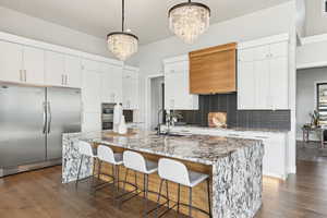 Kitchen featuring a sink, dark wood-style floors, appliances with stainless steel finishes, an inviting chandelier, and decorative backsplash