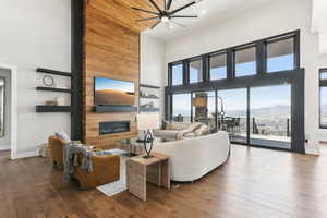 Living area featuring a ceiling fan, a glass covered fireplace, wood-type flooring, baseboards, and a towering ceiling