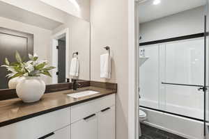 Full bathroom with tile patterned flooring, toilet, vanity, and bath / shower combo with glass door