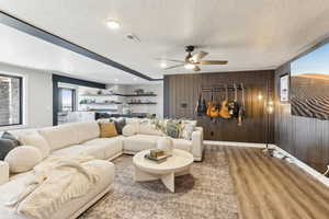Living room with visible vents, a ceiling fan, a textured ceiling, wood finished floors, and wooden walls